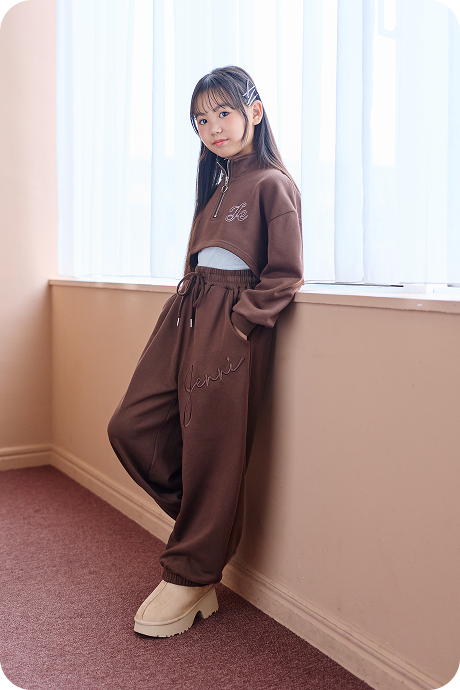 ブラウンのセットアップを着て窓辺に立つ女の子