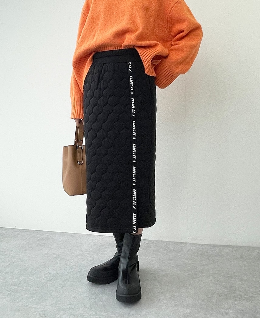 キルトロゴテープスカートを着用し、立っている女性の写真