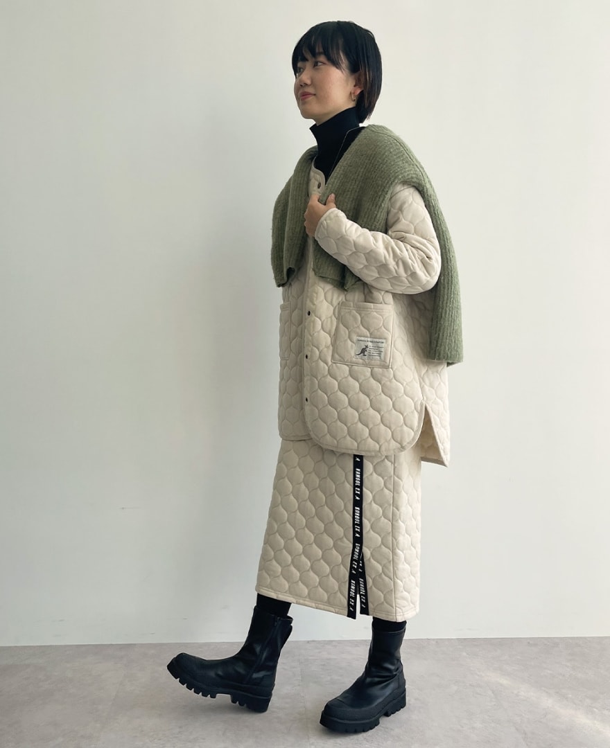 キルトラウンドヘムコートとキルトロゴテープスカートを着用した女性の写真
