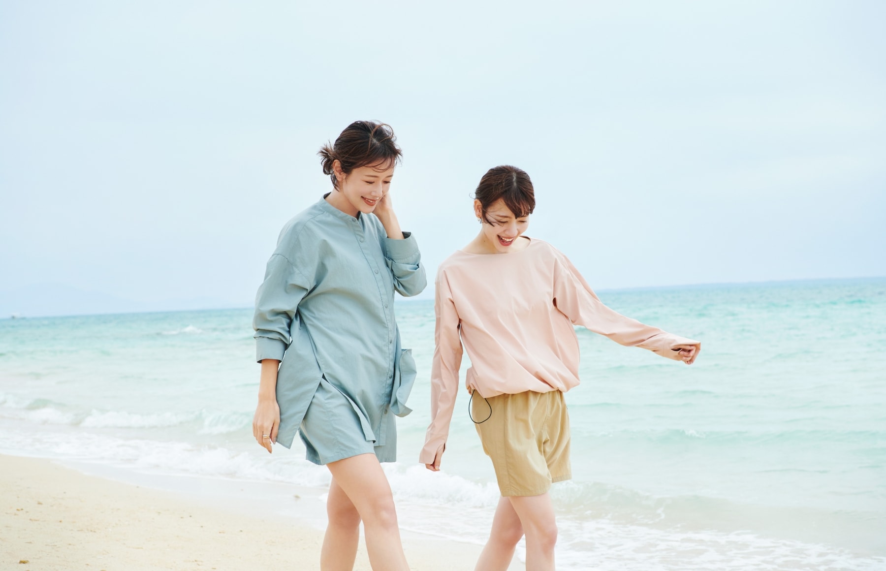 ドロストヘムラッシュガードとラッシュガードショートパンツとラッシュガードシャツを着用した女性二人が談笑しながら砂浜を歩いている写真１