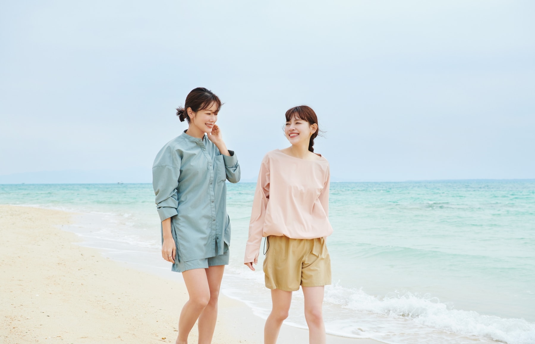 ドロストヘムラッシュガードとラッシュガードショートパンツとラッシュガードシャツを着用した女性二人が談笑しながら砂浜を歩いている写真２