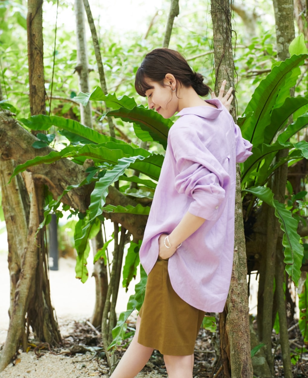 LINENシャツとコットンリネンショートパンツを着用した女性が木に手をついて下を向いている写真