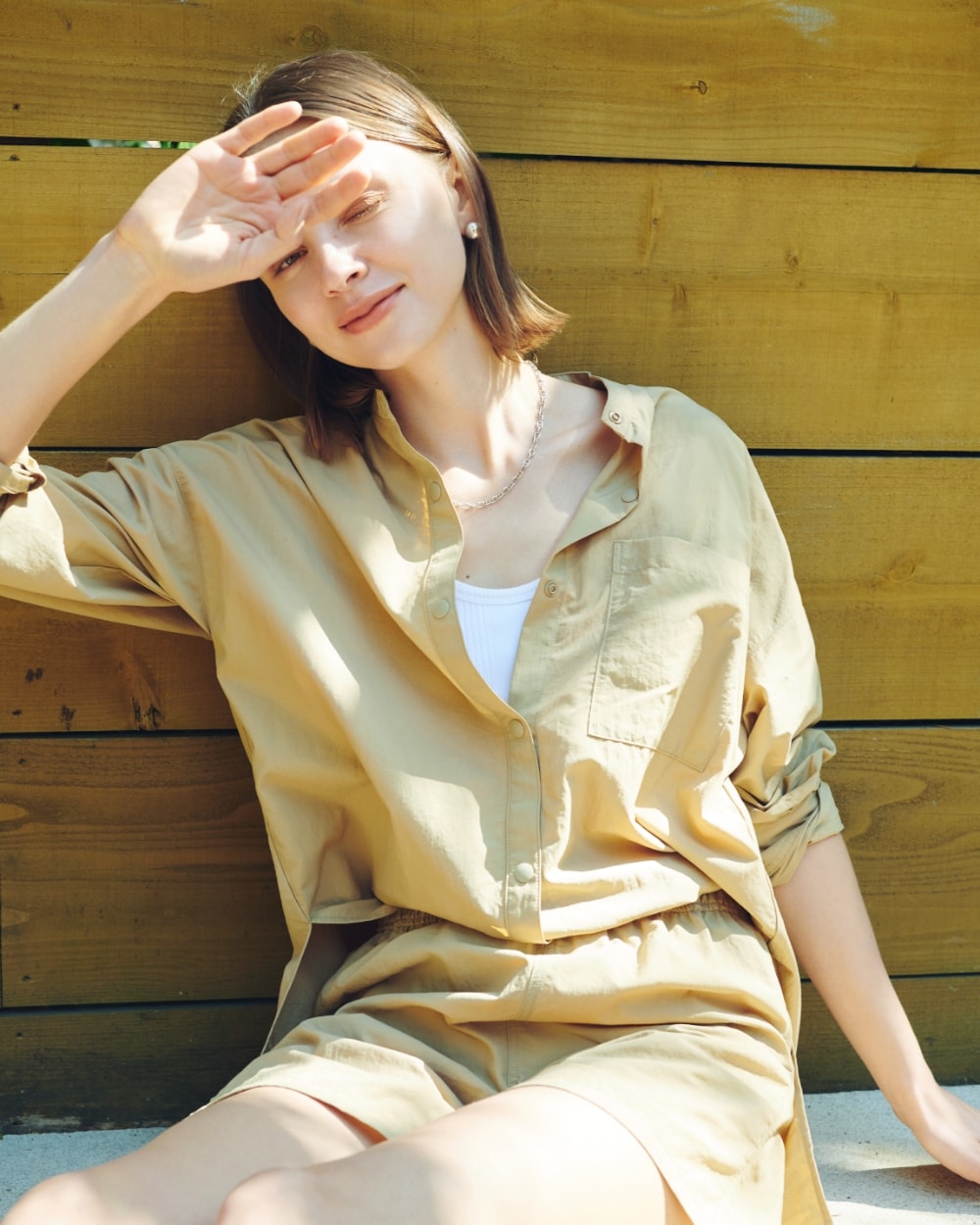 ラッシュガードシャツとラッシュガードショートパンツを着用した女性が地面に座って片手で日除けしている写真