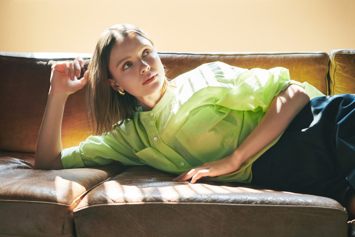 コットンシルクシアーシャツとコットンリネンショートパンツを着用した女性がソファに寝転んでいる写真