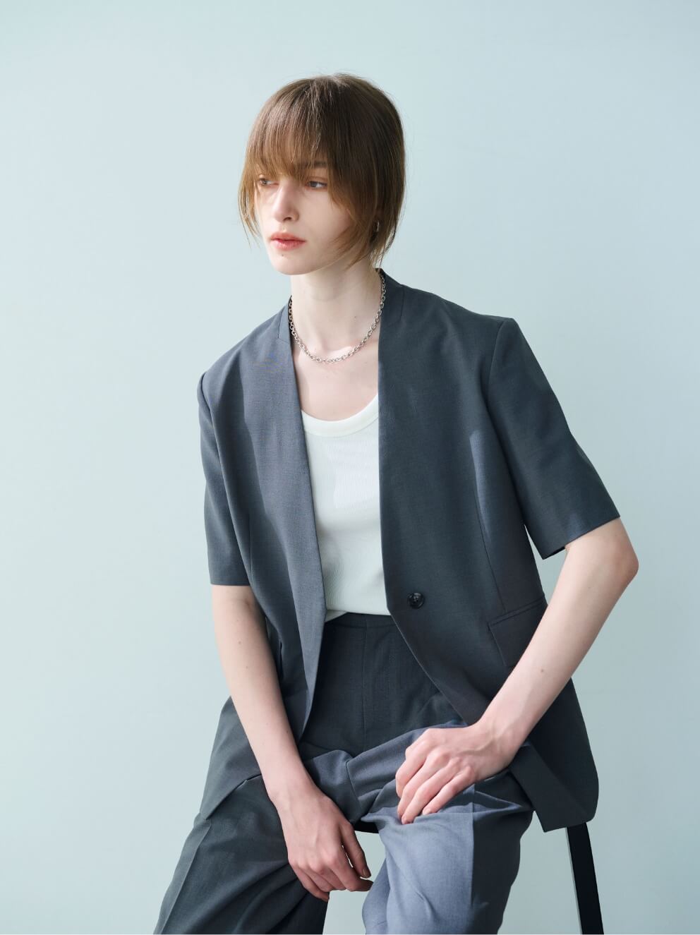 【CLEAN MOTION】ハーフスリーブジャケット、ウォッシャブルバレルパンツ、【AULENTTI】ゴールドバックルレザーベルトを着用して座ってる女性