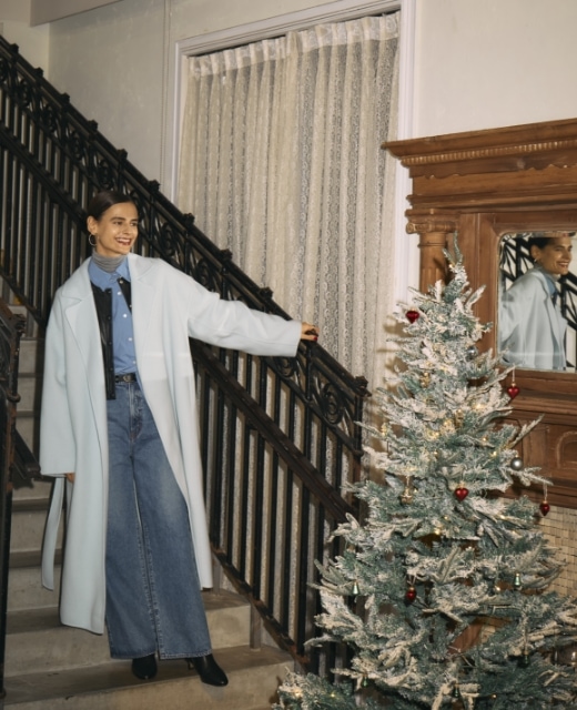 アイスブルーのウールメルトンロングリバーコート・黒のフェイクレザーショートジャケット・ブルーのコンフォータブルシャツ・グレーのメリノウールシアータートル・ミッドブルーの【NEEDBY】ANNIEのフレアデニムを着用した女性が階段上で微笑むビジュアル。