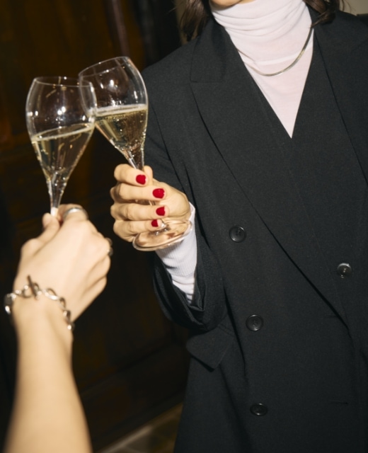 黒のピークドラペルダブルジャケット【CLEAN MOTION】とウォッシャブルオールインワン【CLEAN MOTION】・オフ白のメリノウールシアータートルを着用した女性がシャンパンを片手に乾杯するビジュアル