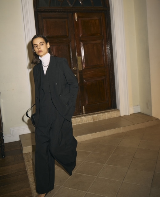 黒のピークドラペルダブルジャケット【CLEAN MOTION】とウォッシャブルオールインワン【CLEAN MOTION】・オフ白のメリノウールシアータートルを着用した女性がドアの前を歩くビジュアル