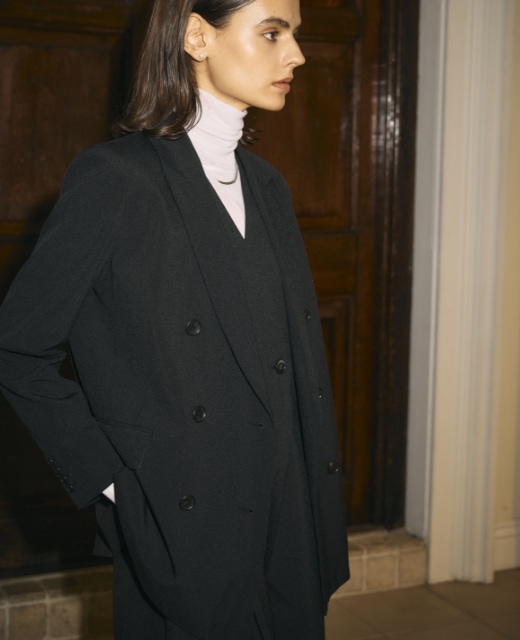 黒のピークドラペルダブルジャケット【CLEAN MOTION】のポケットに手を入れて立つ女性のビジュアル　