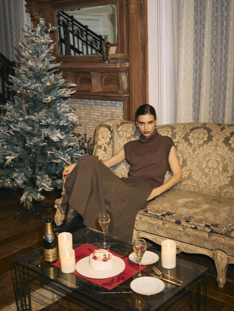 シルクコットンオフタートルニットとウォッシャブルマチフレアスカート【CLEAN MOTION】のブラウンコーディネートでダマスク柄のソファに腰掛ける女性のビジュアル