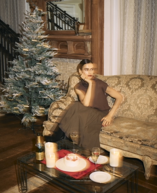 シルクコットンオフタートルニットとウォッシャブルマチフレアスカート【CLEAN MOTION】のブラウンコーディネートで頬杖をついてソファに座る女性のビジュアル