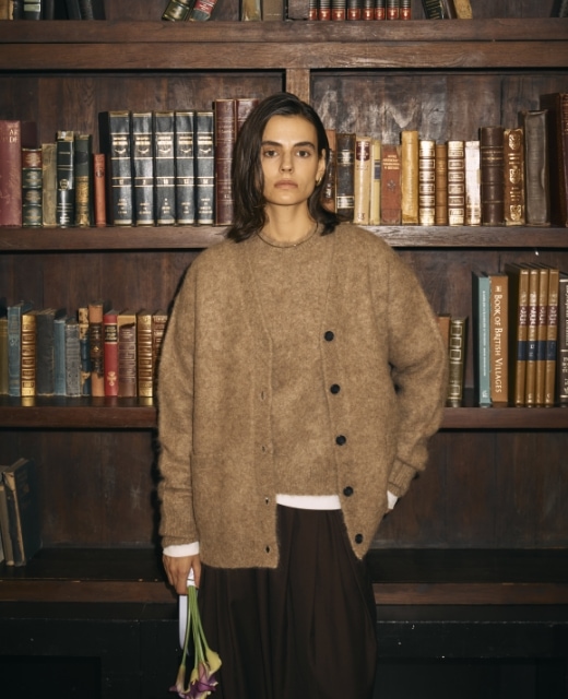 ブラウンのアルパカシャギーニットカーディガンとアルパカシャギーニットプルオーバー、黒のウールライクボリュームドロストパンツを着用した女性が、花束を片手に佇むビジュアル