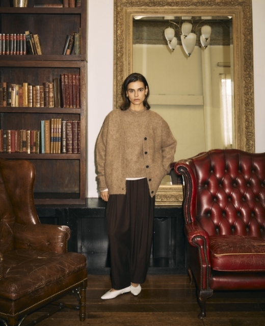 ブラウンのアルパカシャギーニットカーディガンとアルパカシャギーニットプルオーバー、黒のウールライクボリュームドロストパンツを着用した女性がビンテージな鏡の前でポーズをとるビジュアル