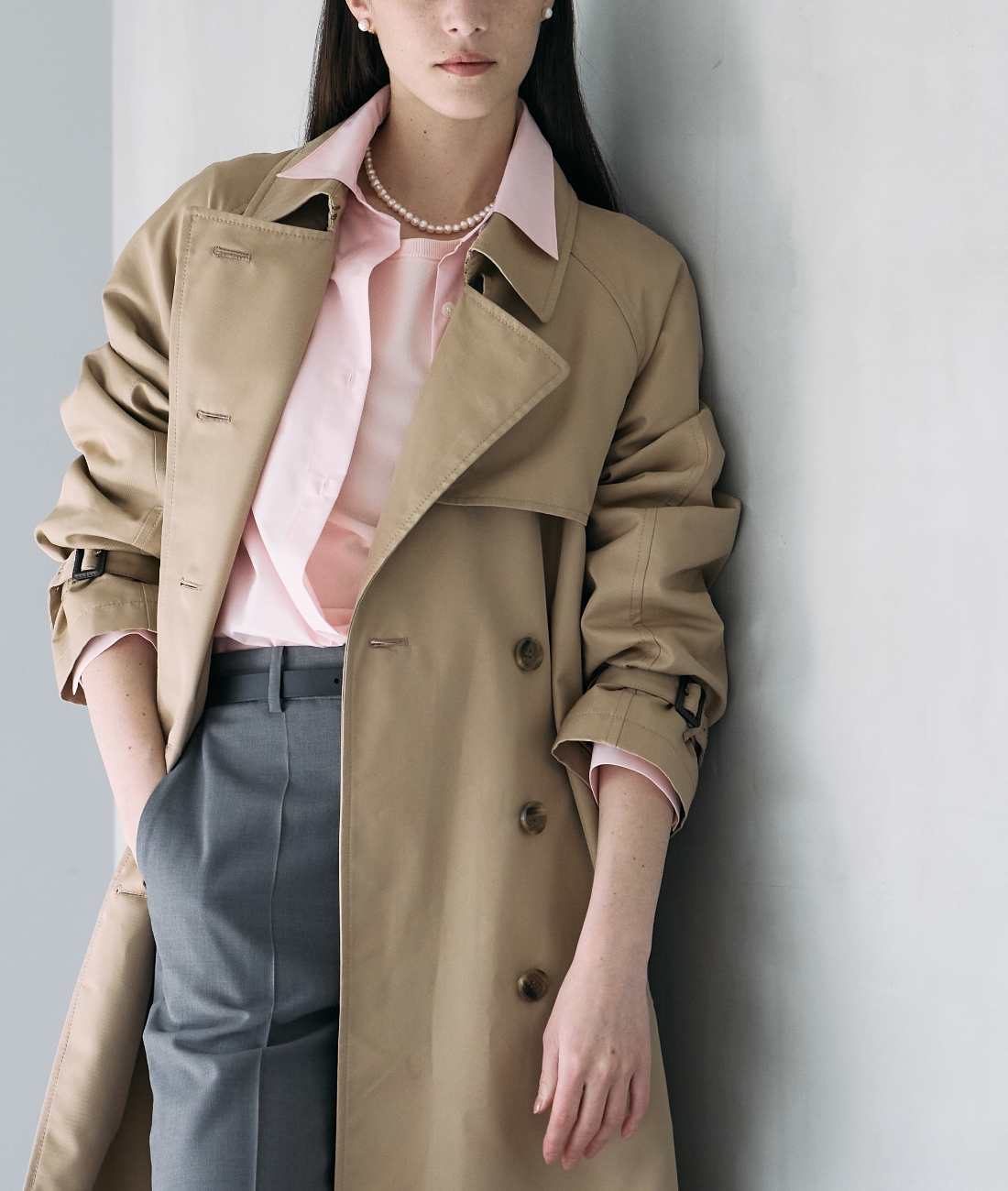 ベージュのロングトレンチコート・ピンクのシャツ・グレーのパンツを着用した女性のアップの画像