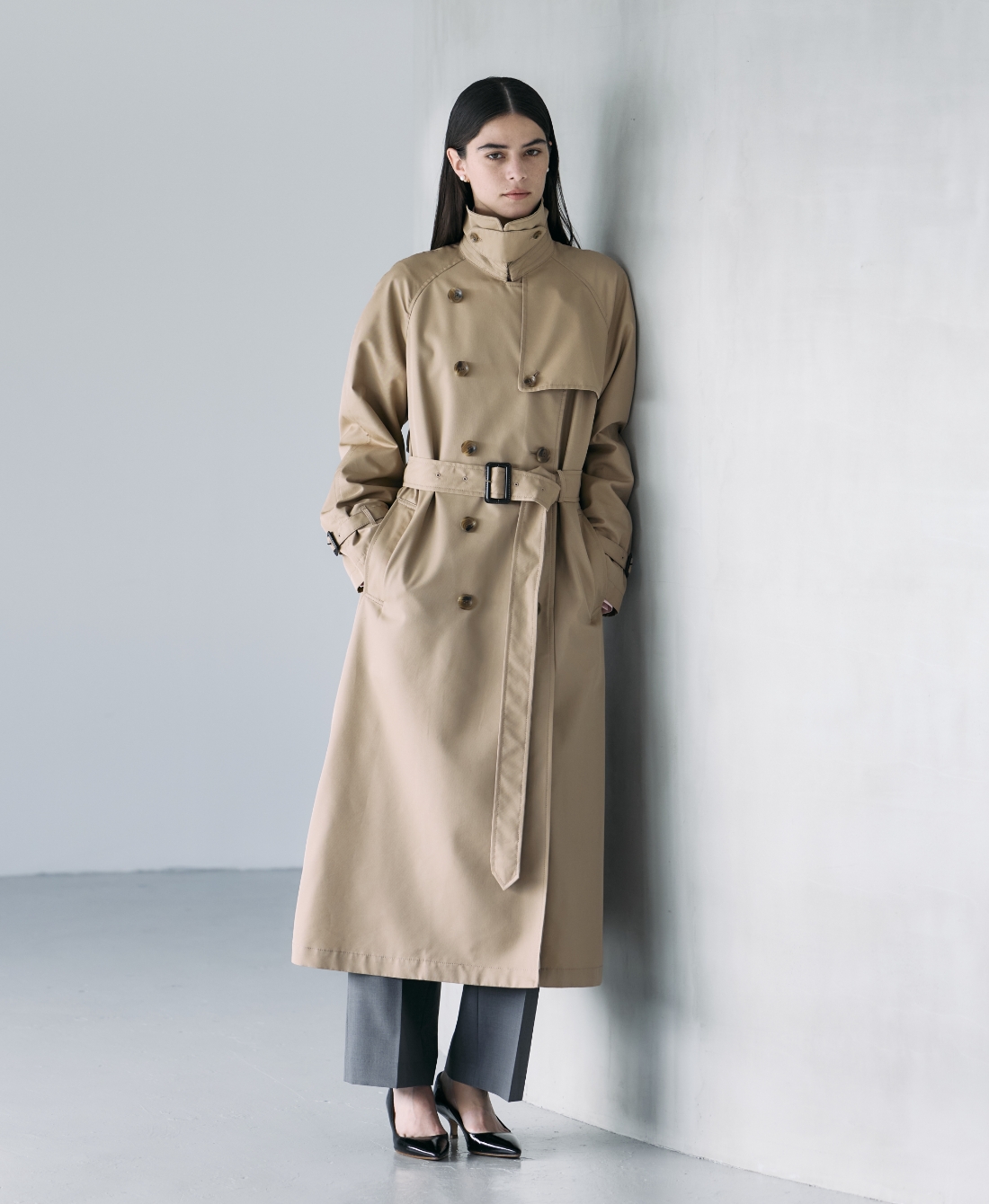 ベージュのロングトレンチコート・グレーのパンツを着用している女性の画像