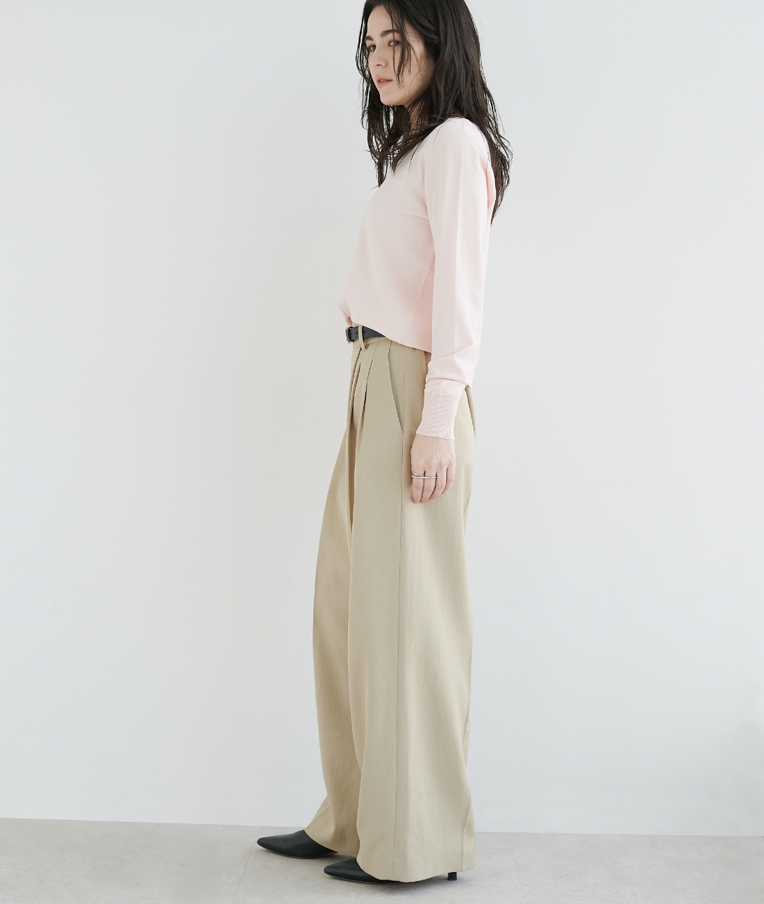 パステルピンクのニット・ベージュの【トリアセリネン】ラップトラウザーパンツを着用している女性の横向きの画像