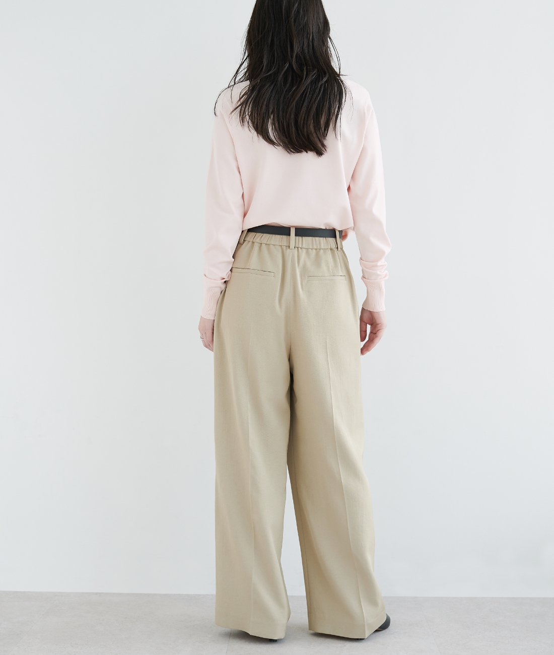 パステルピンクのニット・ベージュの【トリアセリネン】ラップトラウザーパンツを着用している女性の後ろ姿の画像