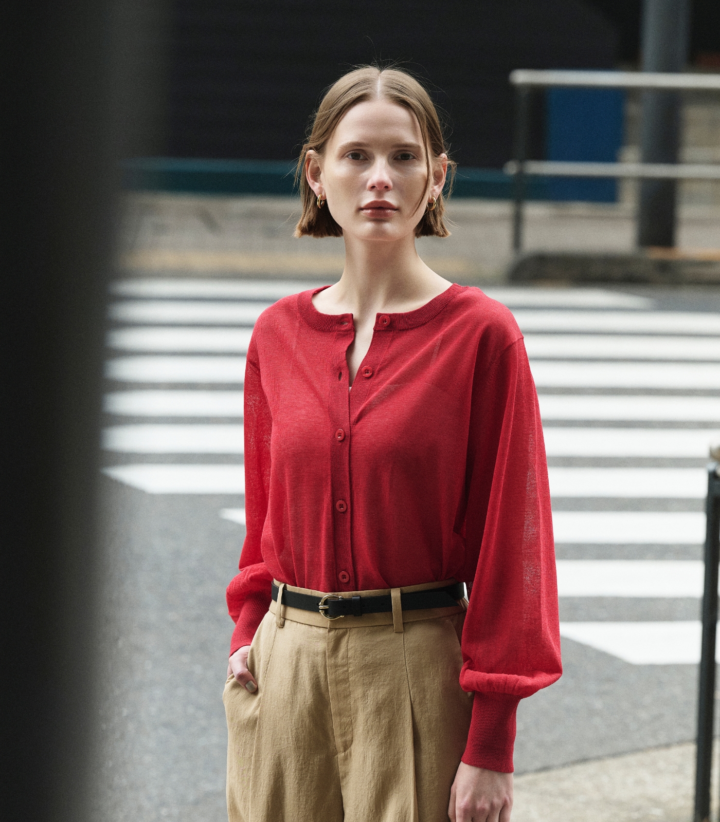 赤色のニットカーディガンとベージュ色のブライトローン撥水フレアパンツを着用した女性１