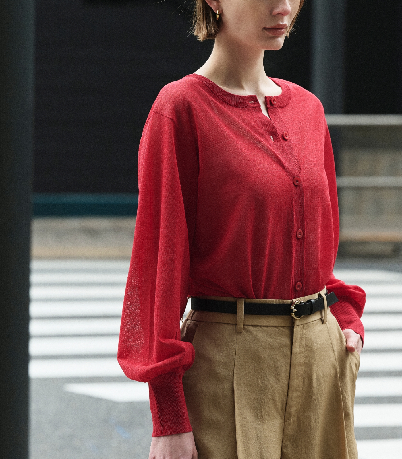赤色のニットカーディガンとベージュ色のブライトローン撥水フレアパンツを着用した女性２