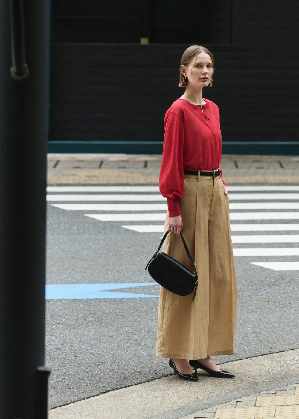 赤色のニットカーディガンとベージュ色のブライトローン撥水フレアパンツを着用した女性３