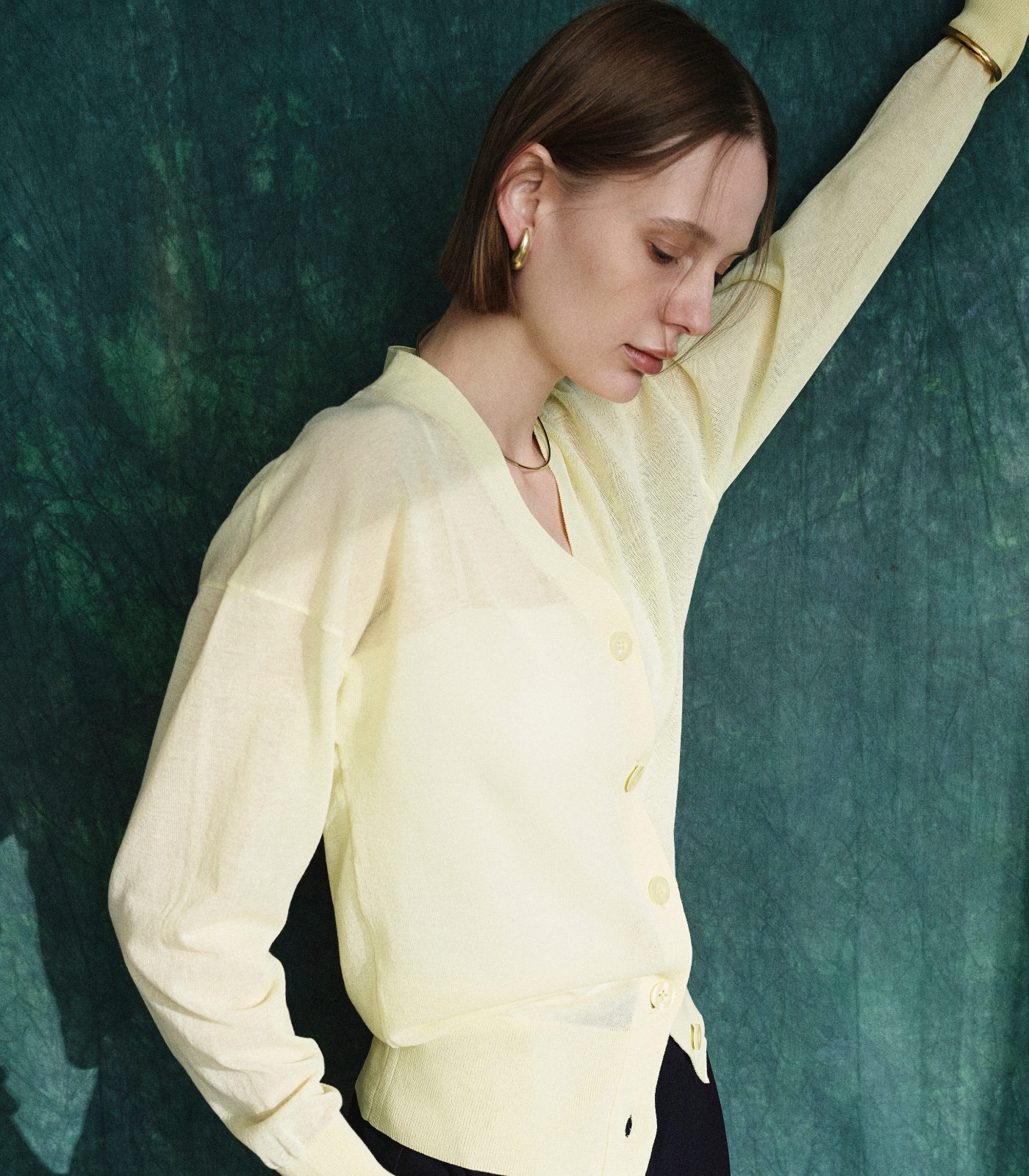 パステルイエロー色のニットカーディガンと黒色のラップトラウザーパンツを着用した女性１