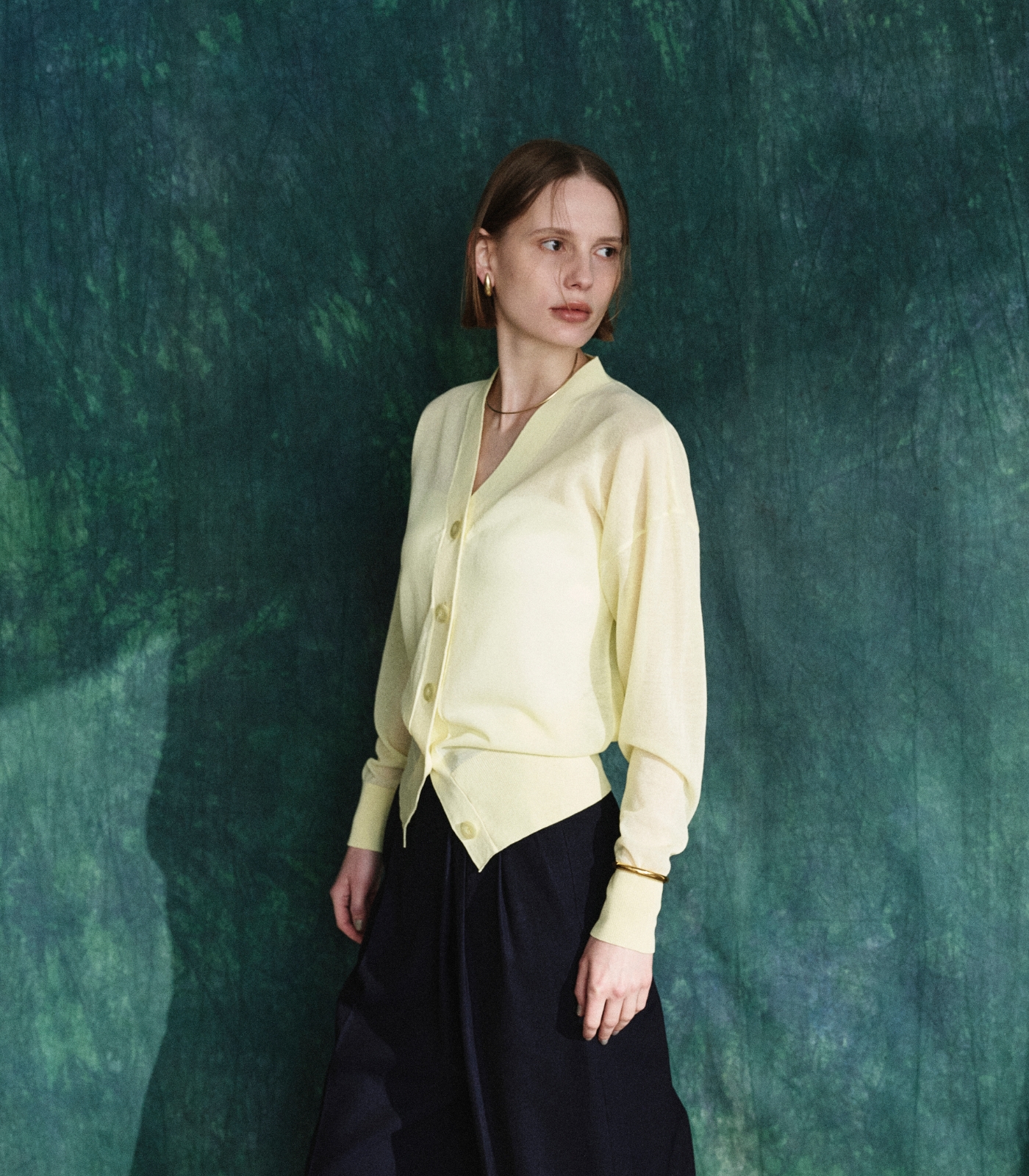 パステルイエロー色のニットカーディガンと黒色のラップトラウザーパンツを着用した女性２