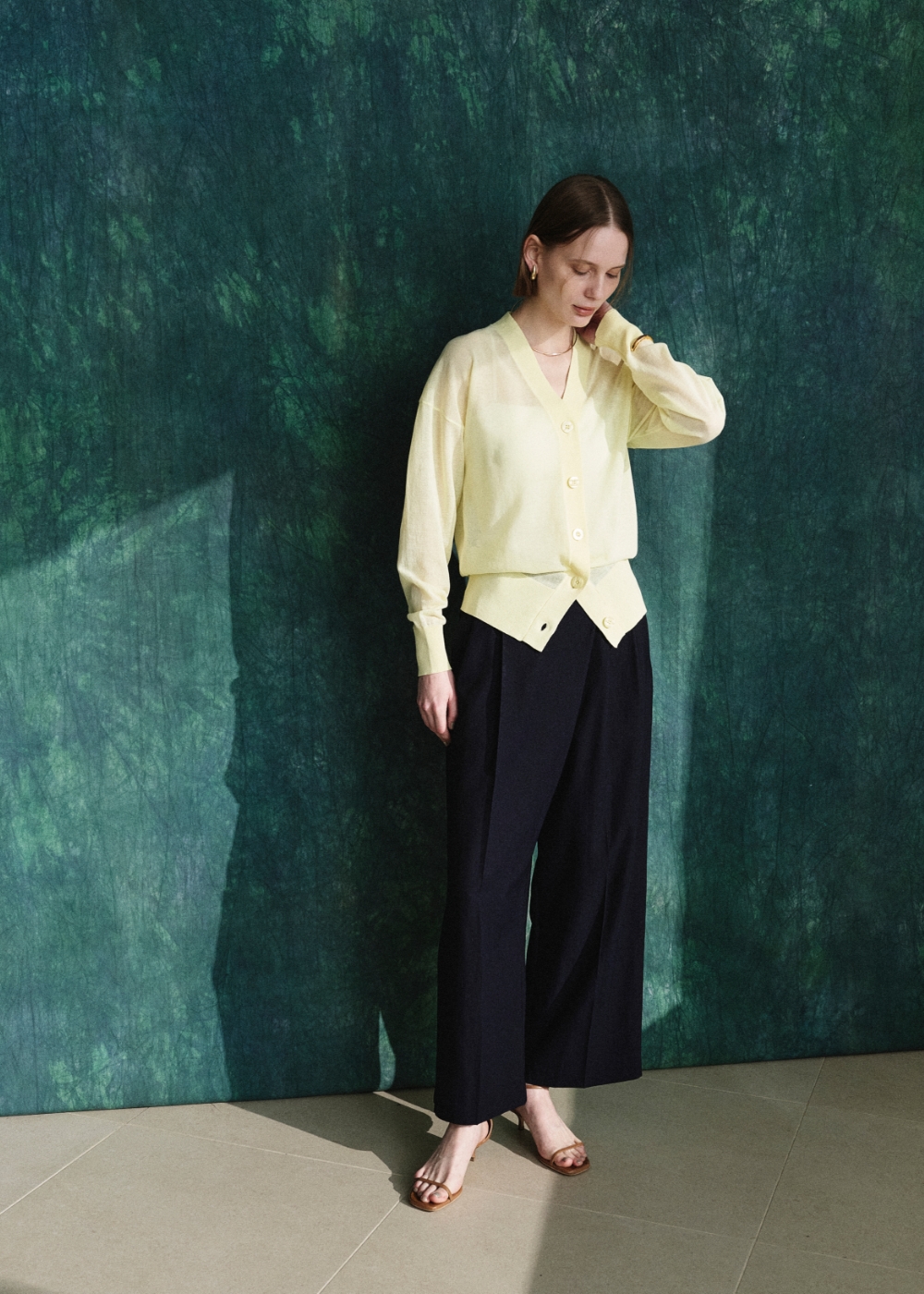 パステルイエロー色のニットカーディガンと黒色のラップトラウザーパンツを着用した女性３