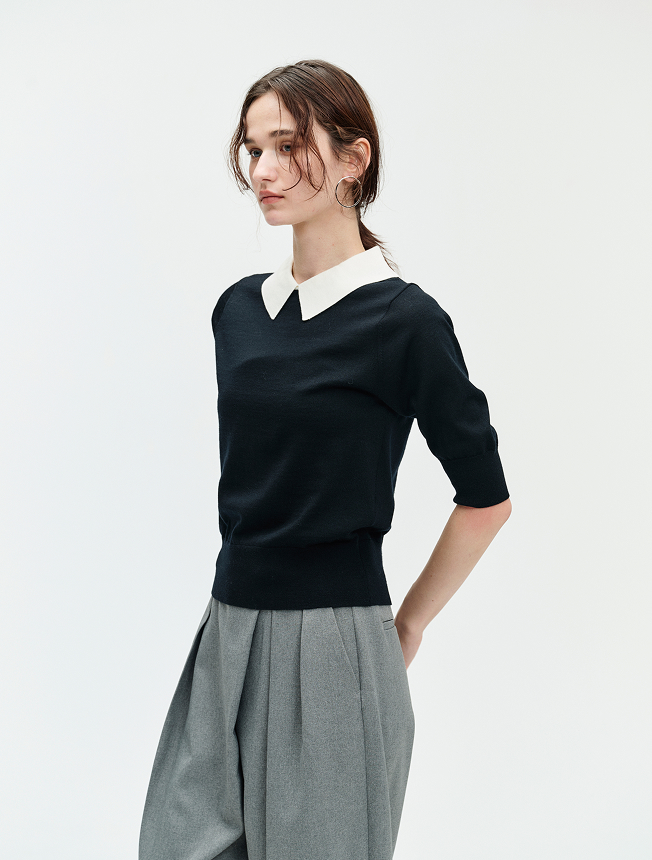 黒い衿付きニットとグレーのパンツを着用した女性