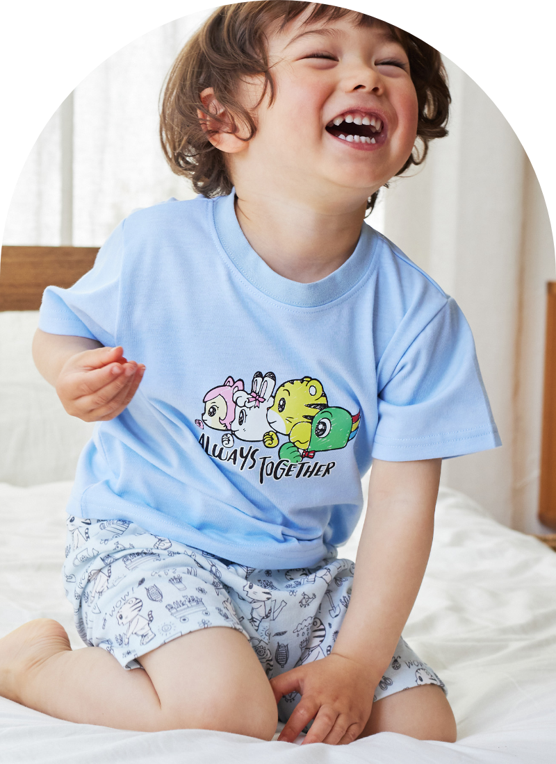しまじろう　プリントパジャマ（かぶりタイプ）を着用した男の子がベッドに座って笑っている写真