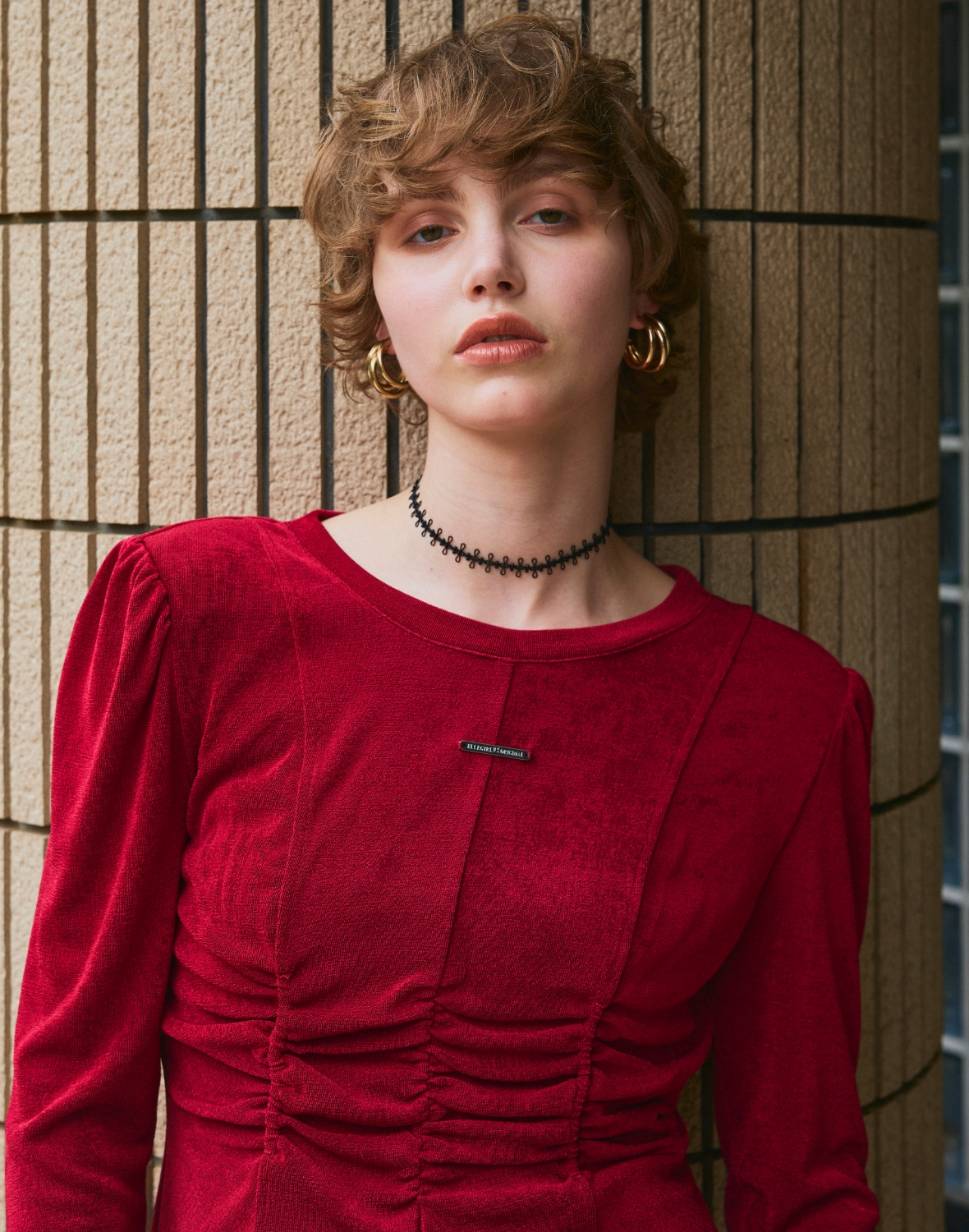 柱の前に立つ赤いTシャツを着た女性の上半身