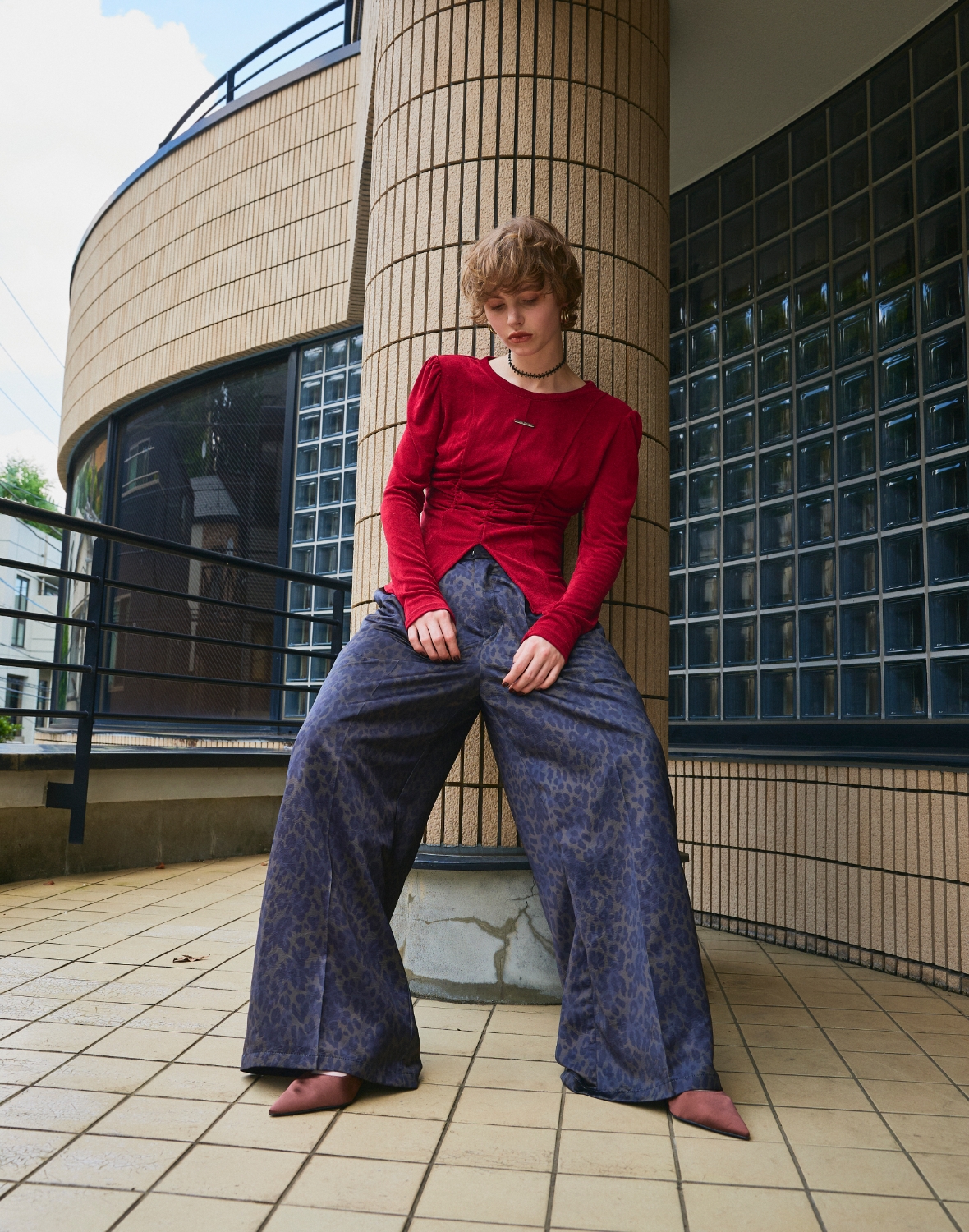 柱の前に足を開いて立つ赤いTシャツを着た女性の全身