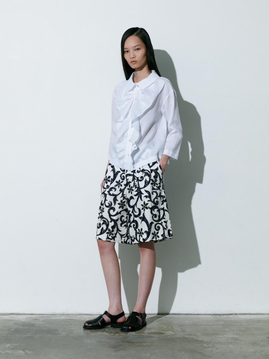 白色のBlouseと黒色の植物模様柄のPantsを着用している女性の画像