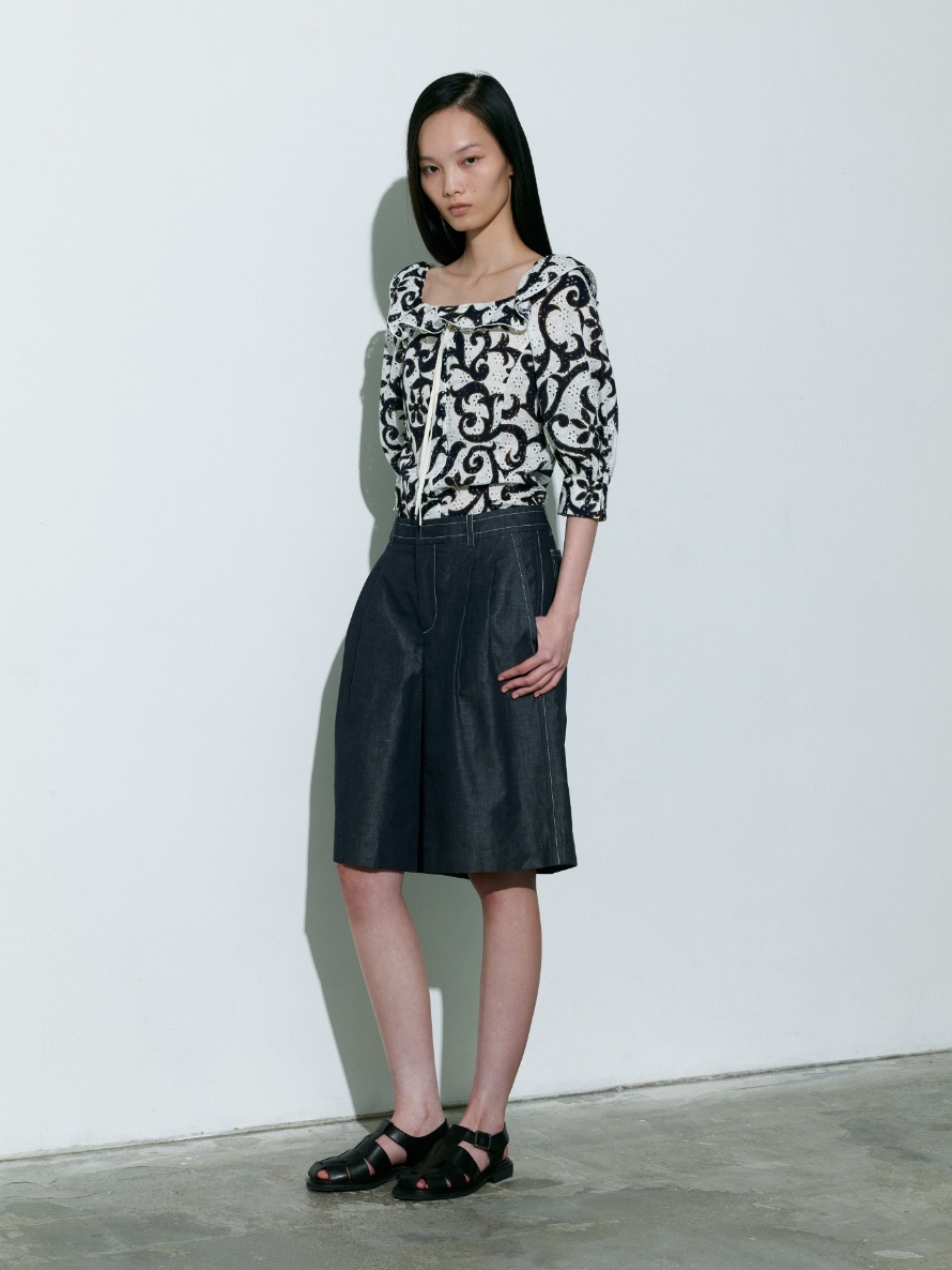 白色背景で黒色の植物模様柄のBlouseと半ズボンを着用している女性の画像