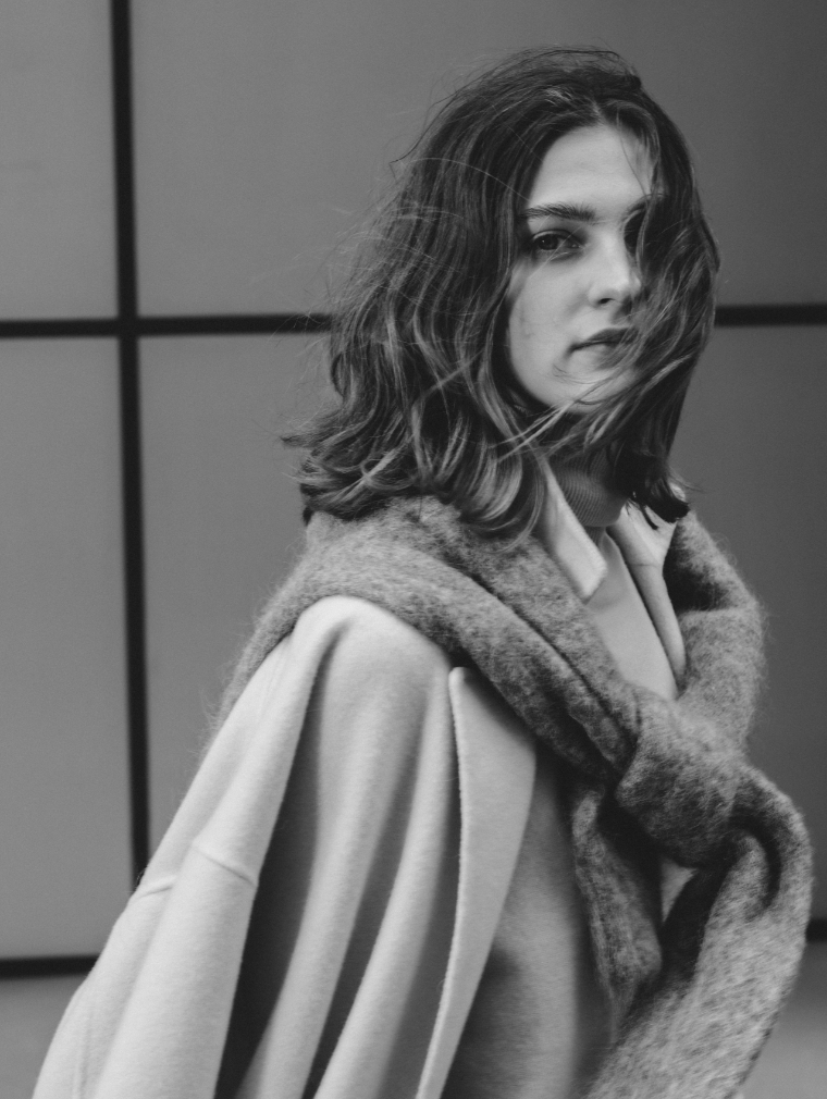ライトブルーのコート・グレーのニット・ライトブルーのトップスを着用した女性のモノクロ画像