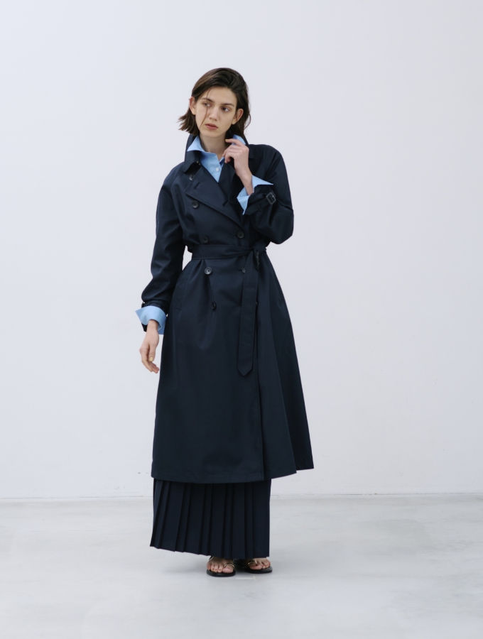 ロングトレンチコートとサックスブルー色のコンフォータブルシャツ、ネイビー色のプリーツスカート【CLEAN MOTION】を着用した女性の画像