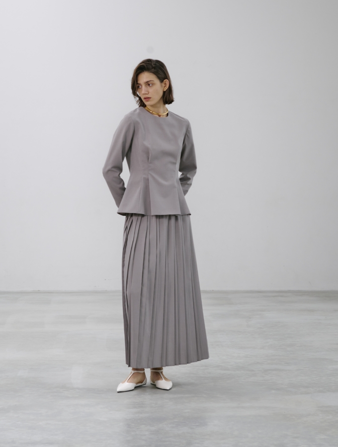 グレージュ色のウォッシャブルペプラムブラウス【CLEAN MOTION】とプリーツスカート【CLEAN MOTION】を着用した女性の画像01