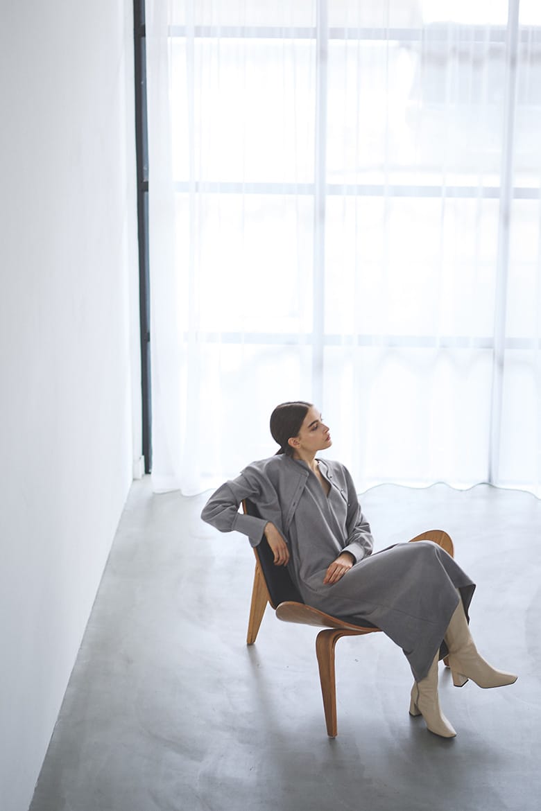 灰色のワンピースを着用し、椅子に腰がけている女性の写真